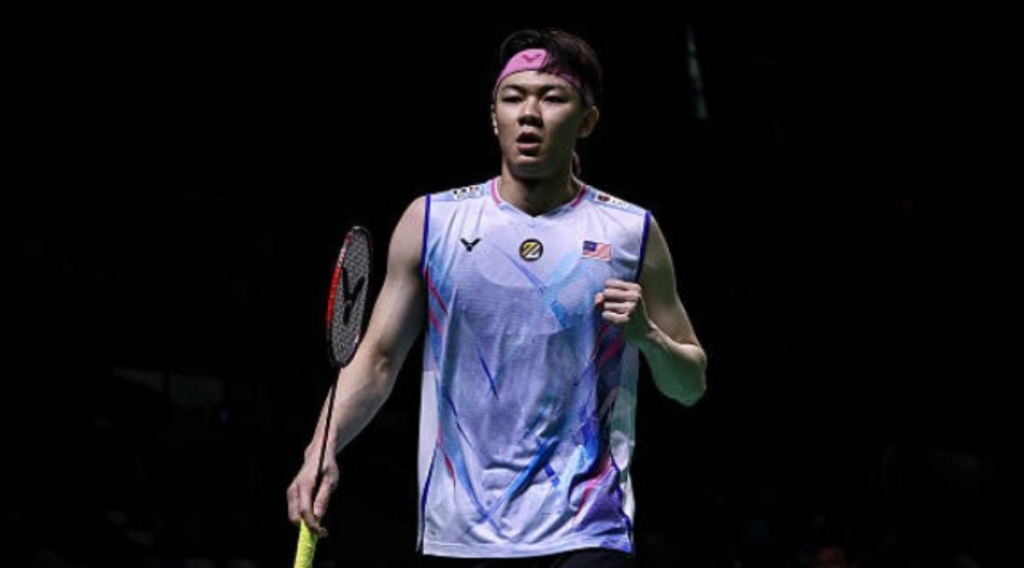 A high-action shot of Lee Zii Jia mid-smash on the badminton court, wearing the Malaysian national team jersey during the 2026 Thomas Cup.