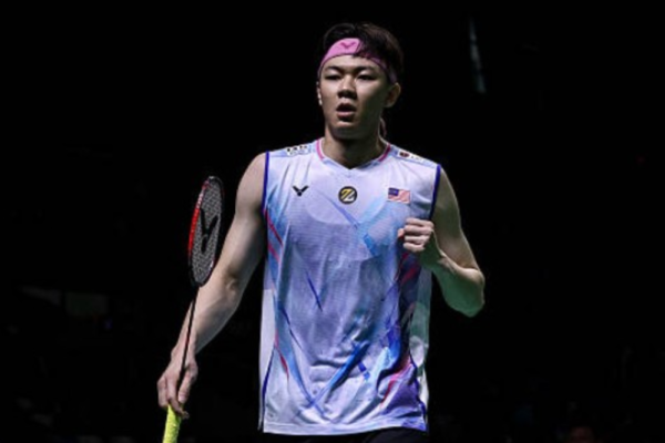 A high-action shot of Lee Zii Jia mid-smash on the badminton court, wearing the Malaysian national team jersey during the 2026 Thomas Cup.