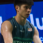 Close-up portrait of Malaysian badminton player Leong Jun Hao wearing a dark green athletic jersey with the national flag emblem during a match.