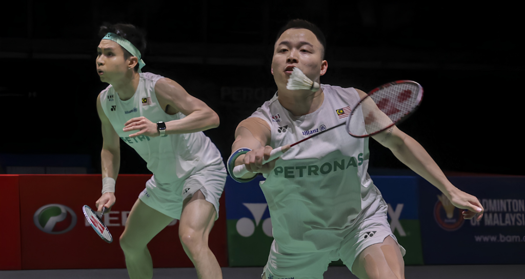 Aaron-Wooi Yik Reunion showing Soh Wooi Yik crouching low at the net with Aaron Chia watching in the background.