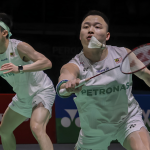 Aaron-Wooi Yik Reunion showing Soh Wooi Yik crouching low at the net with Aaron Chia watching in the background.