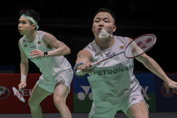 Aaron-Wooi Yik Reunion showing Soh Wooi Yik crouching low at the net with Aaron Chia watching in the background.
