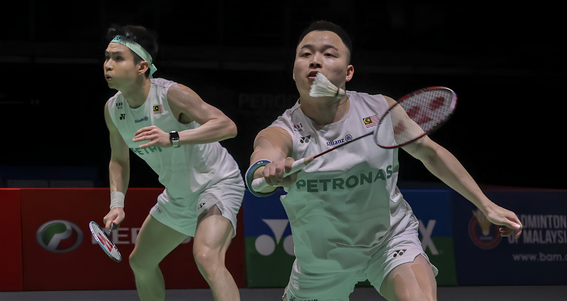 Aaron-Wooi Yik Reunion showing Soh Wooi Yik crouching low at the net with Aaron Chia watching in the background.