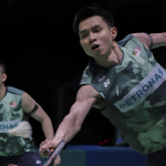 Soh Wooi Yik lunges forward to return a shot while partner Aaron Chia stays alert in their dark green Petronas jerseys.