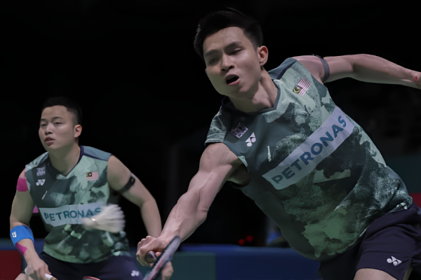 Soh Wooi Yik lunges forward to return a shot while partner Aaron Chia stays alert in their dark green Petronas jerseys.