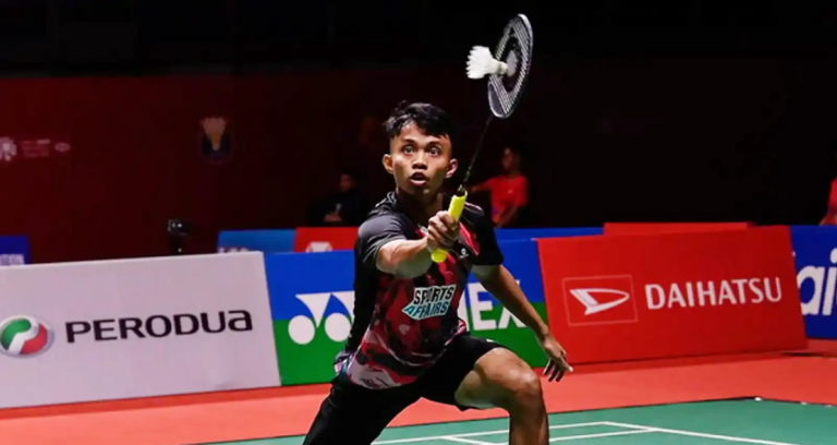 Aidil Sholeh Ali Sadikin lunges forward to execute a forehand net return in his black and red jersey during a match.