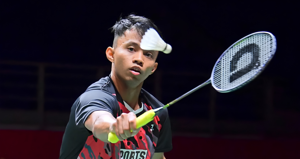 Aidil Sholeh Ali Sadikin tracks the shuttlecock intently while preparing a forehand return in his black and red Sports Affairs jersey