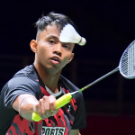 Aidil Sholeh Ali Sadikin tracks the shuttlecock intently while preparing a forehand return in his black and red Sports Affairs jersey