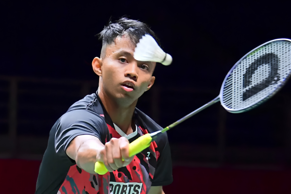 Aidil Sholeh Ali Sadikin tracks the shuttlecock intently while preparing a forehand return in his black and red Sports Affairs jersey