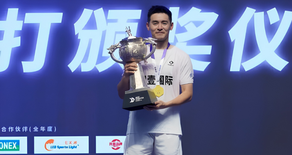Cheam June Wei poses on the podium holding the silver trophy, gold medal, and championship prize money check at the 2026 Lin Dan Cup in Jincheng, China.