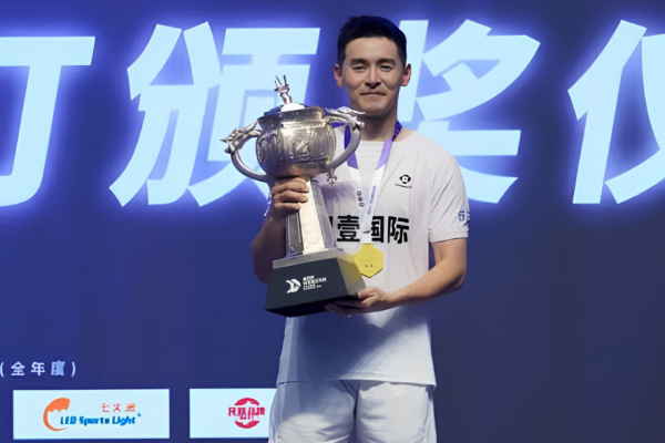 Cheam June Wei poses on the podium holding the silver trophy, gold medal, and championship prize money check at the 2026 Lin Dan Cup in Jincheng, China.