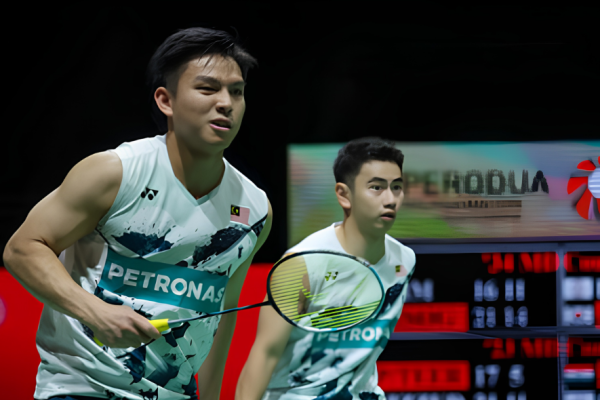 Goh Sze Fei and Nur Izzuddin Rumsani prepare to return a shot in their white Petronas Malaysian national jerseys during an international badminton match.