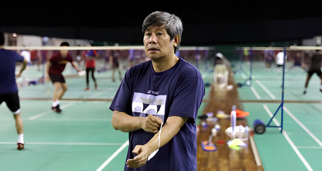 Herry Iman Pierngadi oversees a training session in his navy Yonex t-shirt on the badminton court.