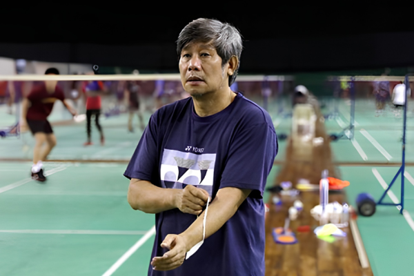Herry Iman Pierngadi oversees a training session in his navy Yonex t-shirt on the badminton court.