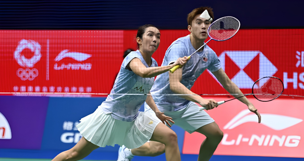 Lai Pei Jing lunges low at the net while Hoo Pang Ron tracks the shuttlecock in their light blue Malaysian kits.