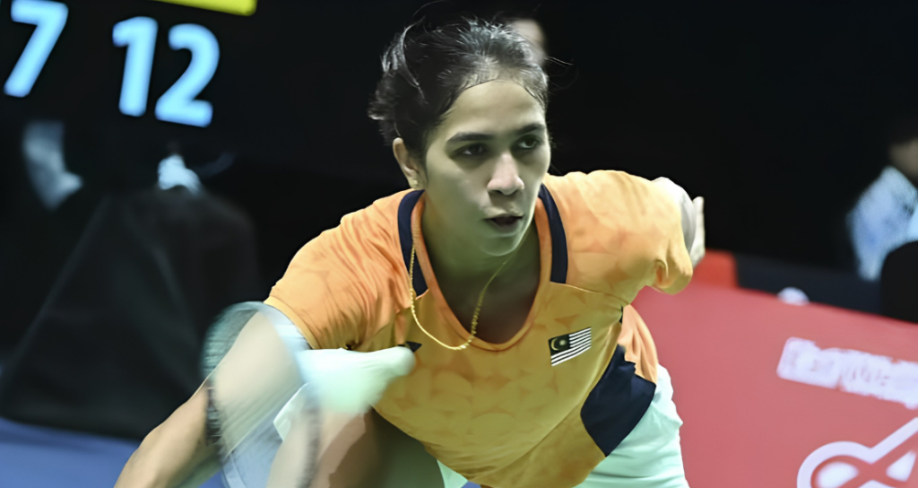 K. Letshanaa lunges forward to execute a low forehand net return in her orange Malaysian national jersey during an international badminton match.