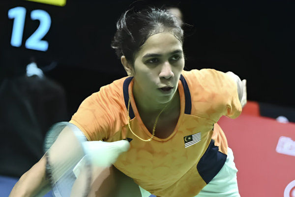 K. Letshanaa lunges forward to execute a low forehand net return in her orange Malaysian national jersey during an international badminton match.