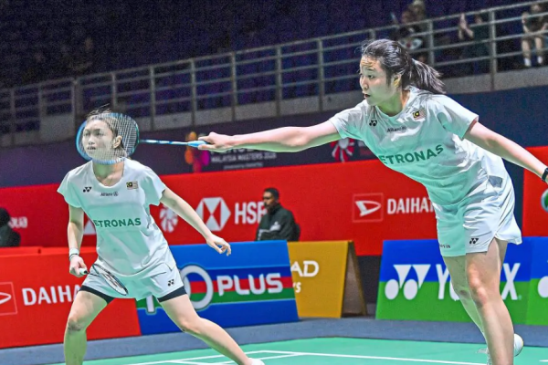 Low Zi Yu stretches to intercept the shuttlecock while partner Noraqilah Maisarah Ramdan watches alertly in their white Petronas jerseys.