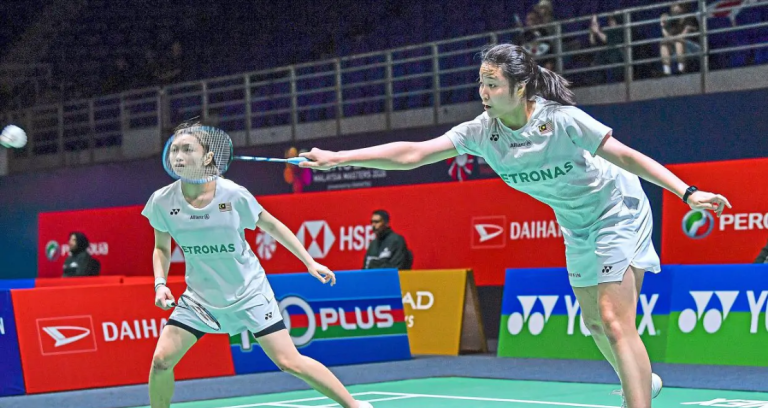 Low Zi Yu stretches to intercept the shuttlecock while partner Noraqilah Maisarah Ramdan watches alertly in their white Petronas jerseys.
