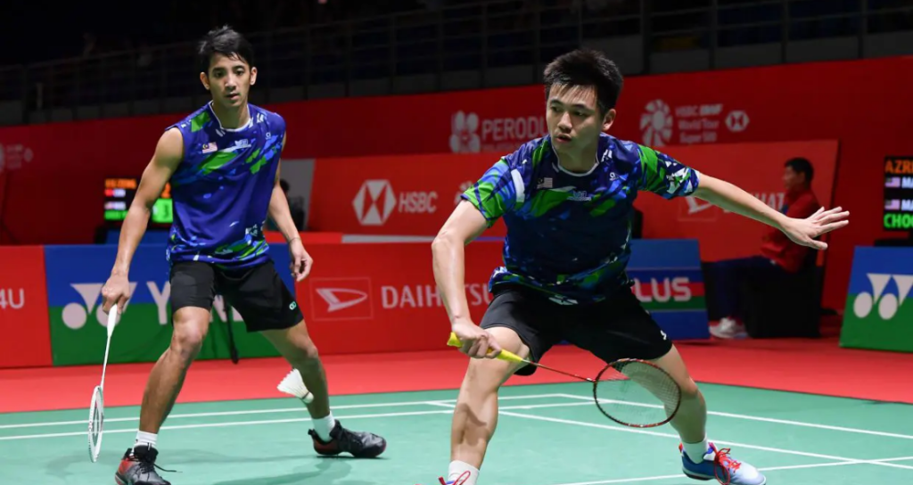 Tan Wee Kiong lunges forward at the net while partner Nur Mohd Azriyn Ayub stays alert in the back court in their blue Malaysian jerseys.
