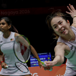 Pearly Tan lunges forward low at the net while M. Thinaah provides back-court cover in their white Malaysian jerseys during the Asian Games.