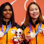 M. Thinaah and Pearly Tan smile on the podium holding their bronze medals and official mascot toys at the Asian Games.