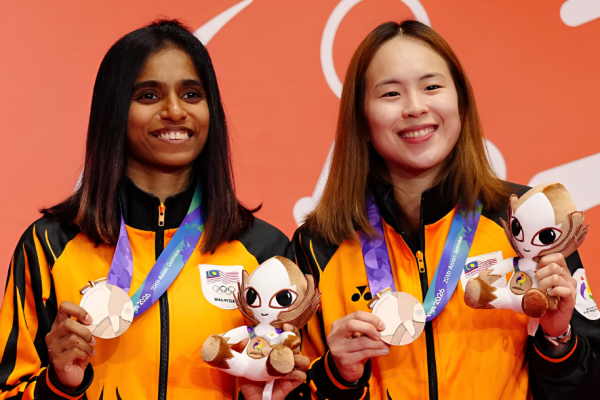 M. Thinaah and Pearly Tan smile on the podium holding their bronze medals and official mascot toys at the Asian Games.