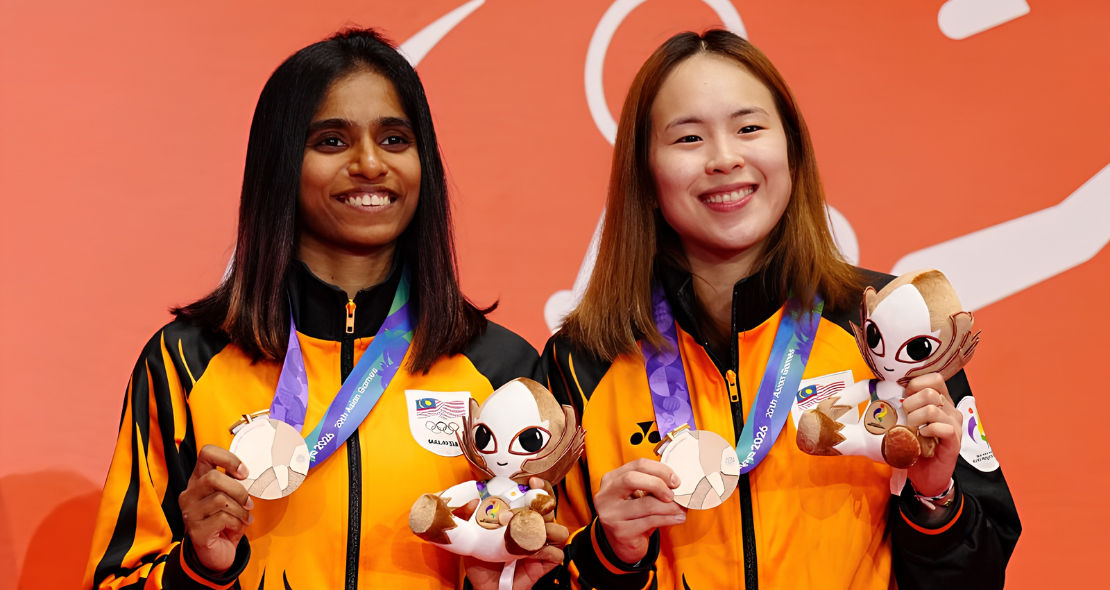 M. Thinaah and Pearly Tan smile on the podium holding their bronze medals and official mascot toys at the Asian Games.