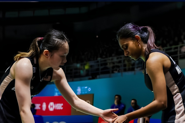 Pearly Tan and M. Thinaah touch hands on court while communicating between rallies in their black Malaysian jerseys.