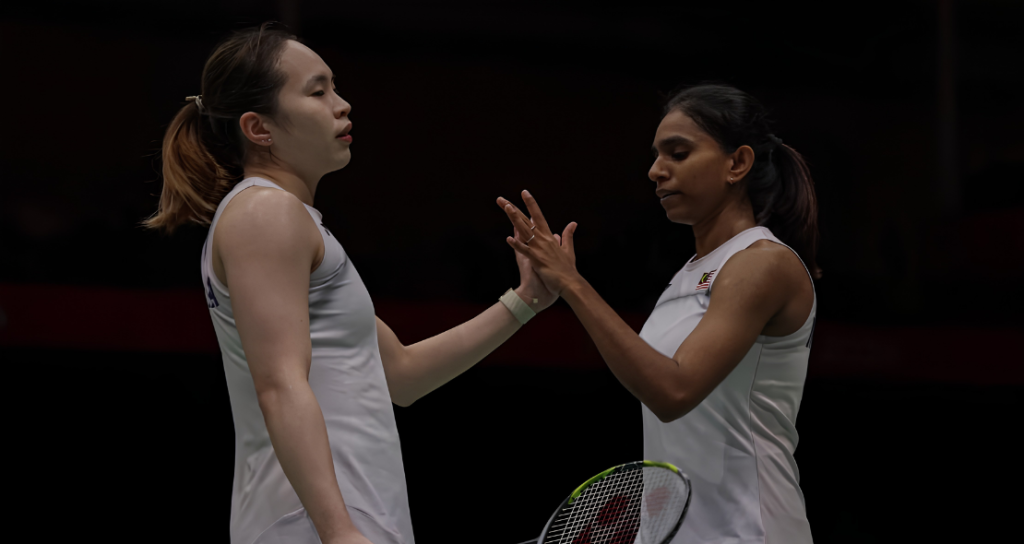 Pearly Tan and M. Thinaah exchange a focused high five in their white Malaysian national jerseys on court.