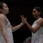 Pearly Tan and M. Thinaah exchange a focused high five in their white Malaysian national jerseys on court.