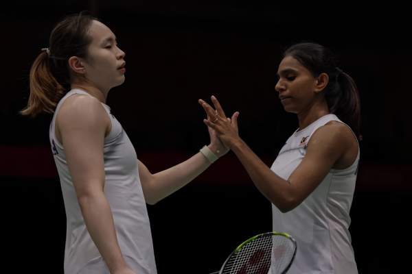 Pearly Tan and M. Thinaah exchange a focused high five in their white Malaysian national jerseys on court.