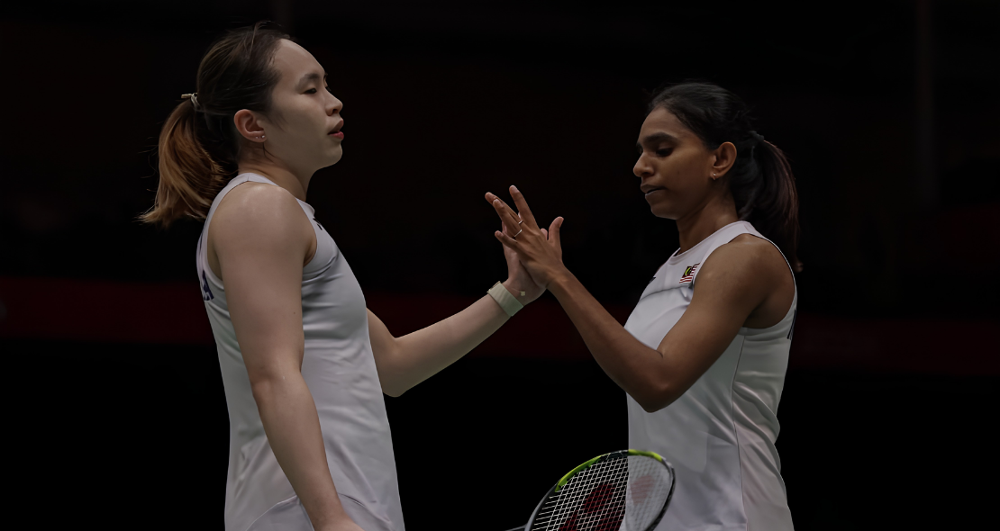 Pearly Tan and M. Thinaah exchange a focused high five in their white Malaysian national jerseys on court.