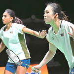 Pearly Tan and M. Thinaah adopt a focused ready stance on court in their white Malaysian jerseys during a match.