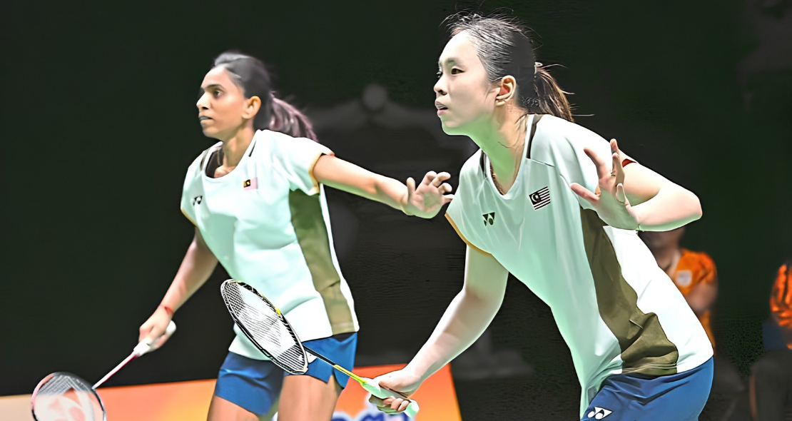 Pearly Tan and M. Thinaah adopt a focused ready stance on court in their white Malaysian jerseys during a match.