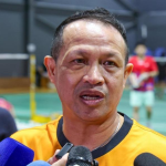 Rexy Mainaky speaks into media microphones during a press interview in his yellow Malaysian national jersey.