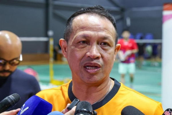 Rexy Mainaky speaks into media microphones during a press interview in his yellow Malaysian national jersey.