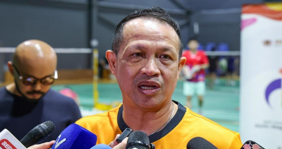 Rexy Mainaky speaks into media microphones during a press interview in his yellow Malaysian national jersey.