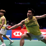 Soh Wooi Yik lunges forward at the net while partner Aaron Tai covers the back court in their yellow Malaysian national jerseys.