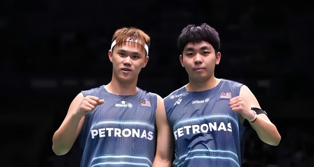 Tee Kai Wun and Yap Roy King pose on court in their navy blue Petronas Malaysia national team jerseys while celebrating with fist pumps.