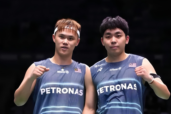 Tee Kai Wun and Yap Roy King pose on court in their navy blue Petronas Malaysia national team jerseys while celebrating with fist pumps.