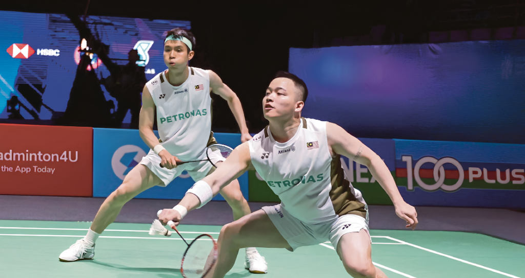 Aaron Chia lunges forward to return a shot while Soh Wooi Yik stays alert in their white Petronas jerseys.