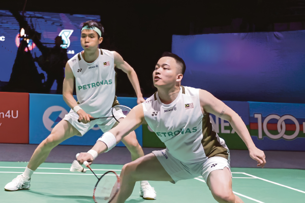 Aaron Chia lunges forward to return a shot while Soh Wooi Yik stays alert in their white Petronas jerseys.
