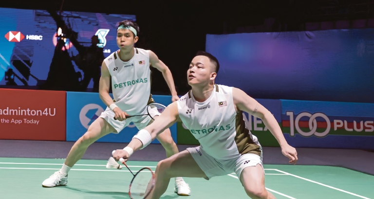 Aaron Chia lunges forward to return a shot while Soh Wooi Yik stays alert in their white Petronas jerseys.