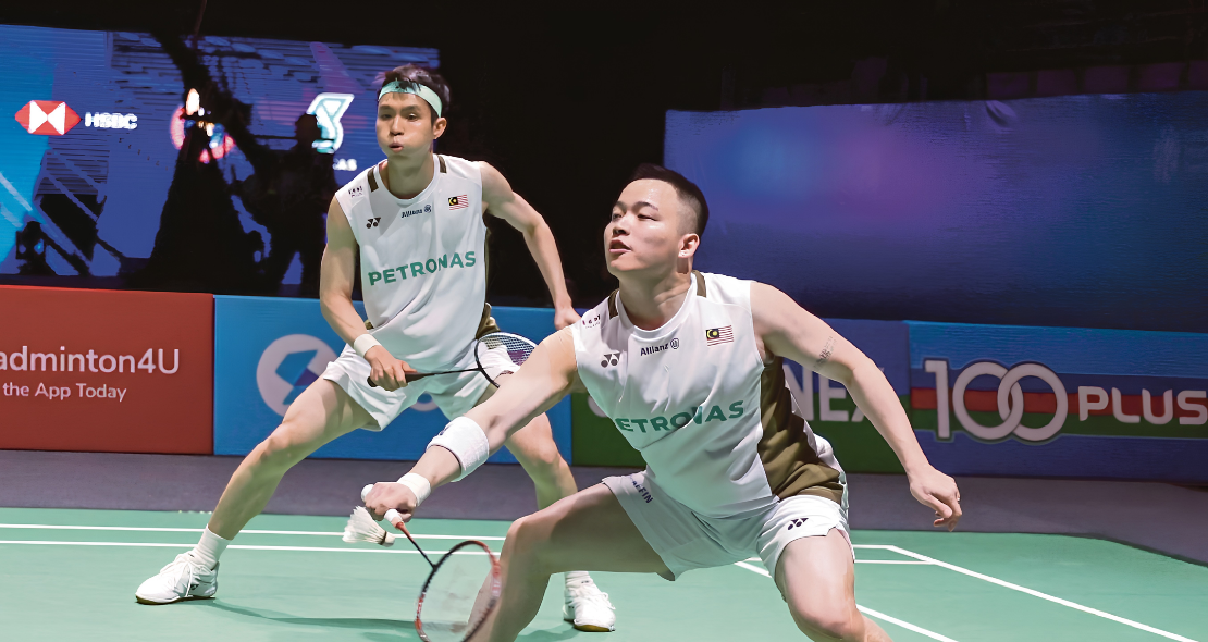Aaron Chia lunges forward to return a shot while Soh Wooi Yik stays alert in their white Petronas jerseys.