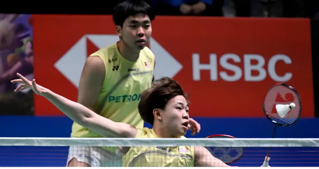 Aaron Tai lunges forward to intercept the shuttlecock at the net while Yap Roy King watches alertly in their yellow Petronas jerseys.