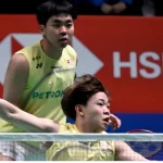 Aaron Tai lunges forward to intercept the shuttlecock at the net while Yap Roy King watches alertly in their yellow Petronas jerseys.