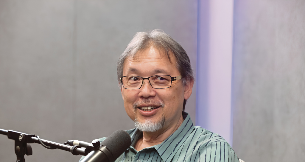 Razif Sidek smiles while speaking into a microphone during a studio podcast interview.