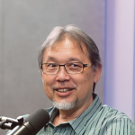 Razif Sidek smiles while speaking into a microphone during a studio podcast interview.