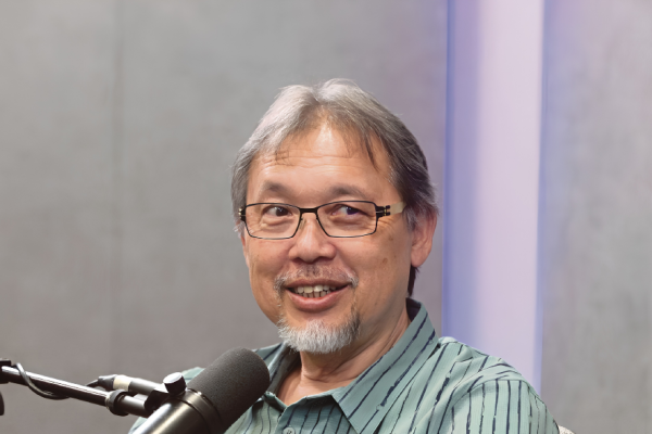 Razif Sidek smiles while speaking into a microphone during a studio podcast interview.